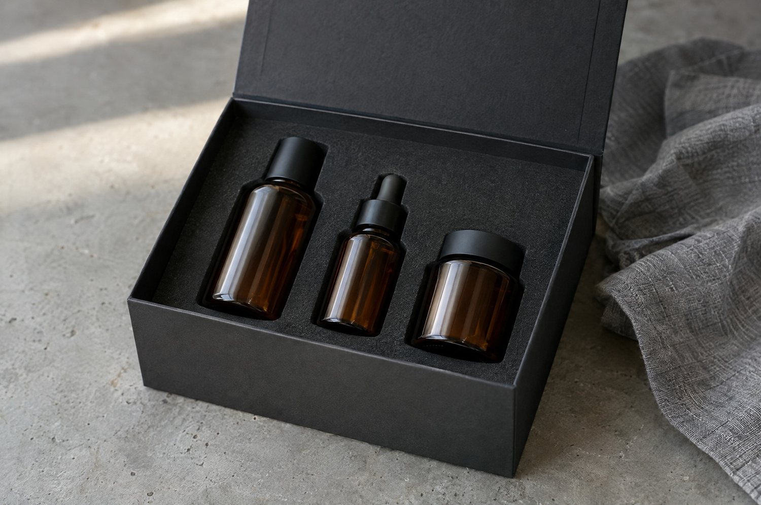 Charcoal magnetic box with a foam insert holding three amber skincare bottles